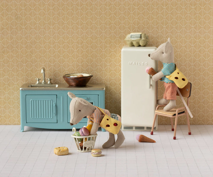 Tableau with brother and siter mice unpacking groceries in the kitchen. Brother mouse is taking food out of the bike basket; sister mouse is putting food away in the refrigerator. 