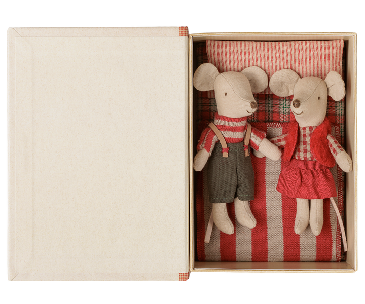 Mouse twins wearing their Christmas outfits inside the story book box lying on a red and off-white striped pillow, red-checked fabric mattress and red and off-white striped blanket.