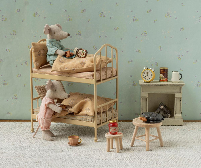 Tableau with one mouse in the upper bunk with a snack and another getting into the lower bunk, next to stools and fireplace.