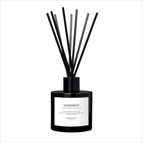 Eight black reeds in a black glass bottle with a white label with the text 'MIDNIGHT.'