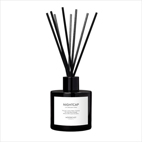 Eight black reeds in a black glass bottle with white label with the text 'NIGHTCAP.'