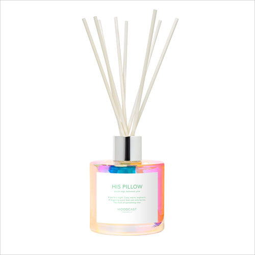 A reed diffuser bottle with an iridescent pastel finish and natural reed sticks, labeled 'HIS PILLOW' by Moodcast.