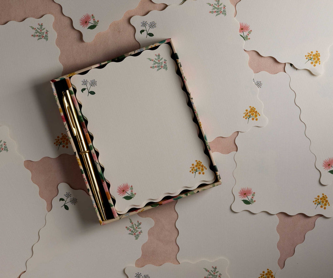 Scalloped pages with a different flower in each corner, in a box with gold pen.