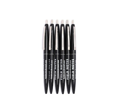 Set of six black pens, with a silver clip and the text 'Field Notes' in white, aligned one beside another.