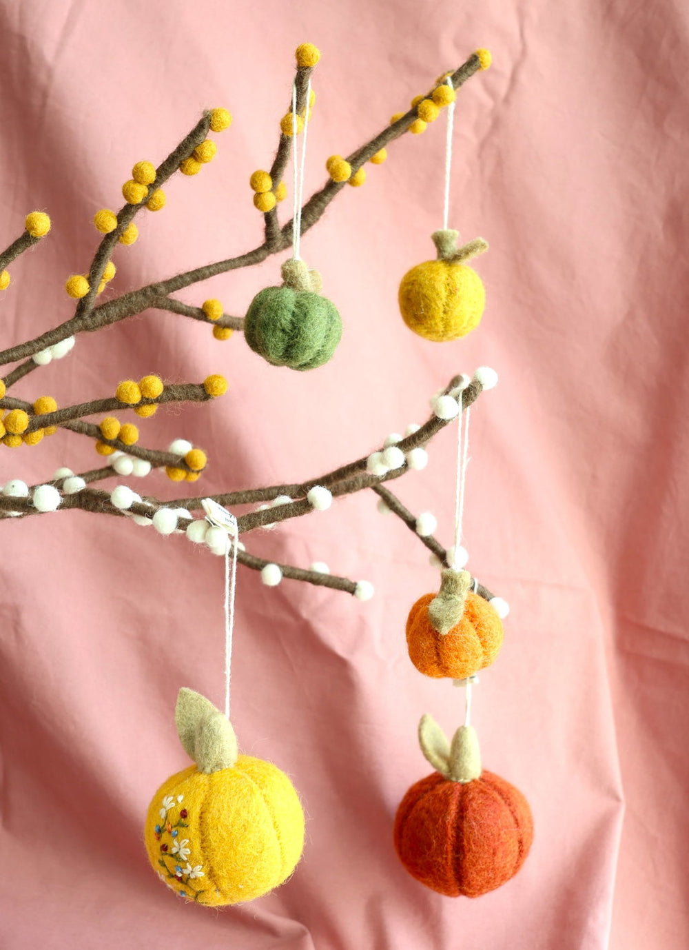 Mini felt pumpkins dangling from felt branches with yellow and white berries. An embroidered yellow felt pumpkin is included in the display.