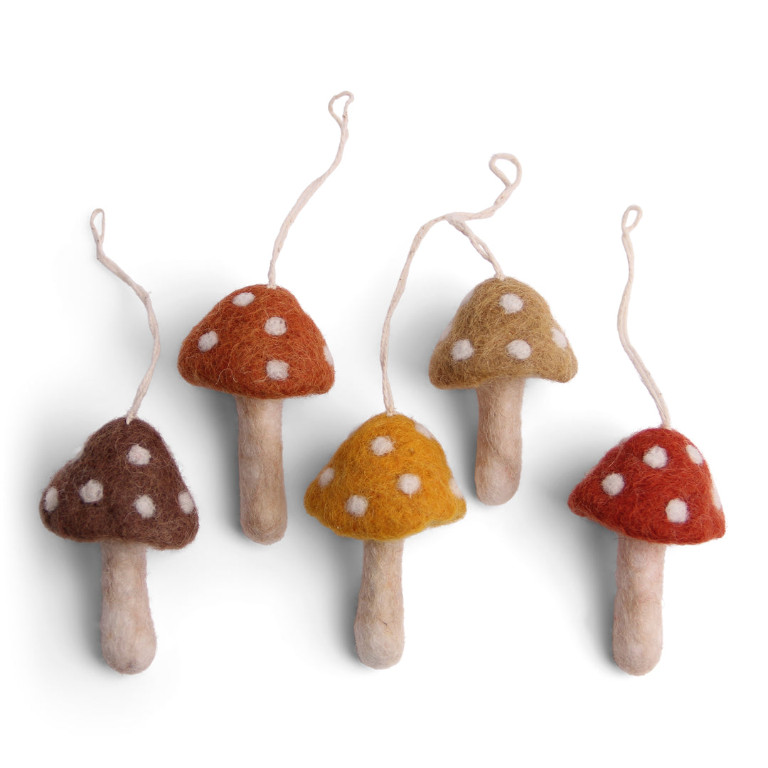 Set of five felt mushroom ornaments in various earth tone colors, each with a string attached to the top.