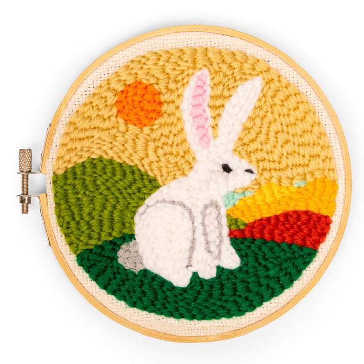Embroidery hoop with a rabbit design against a colorful landscape background