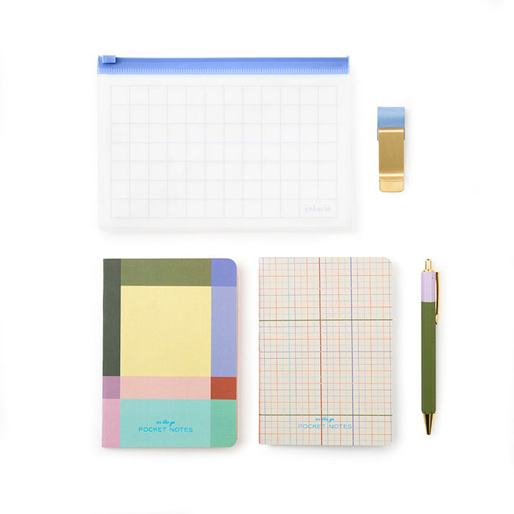 Components of the stationery set: pouch with grid design, pen holder clip, two notebooks, and a pen.