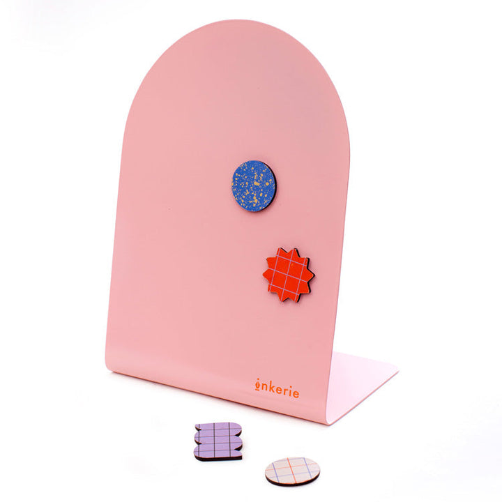 Pink metal memo board with four colorful magnets in fun shapes.