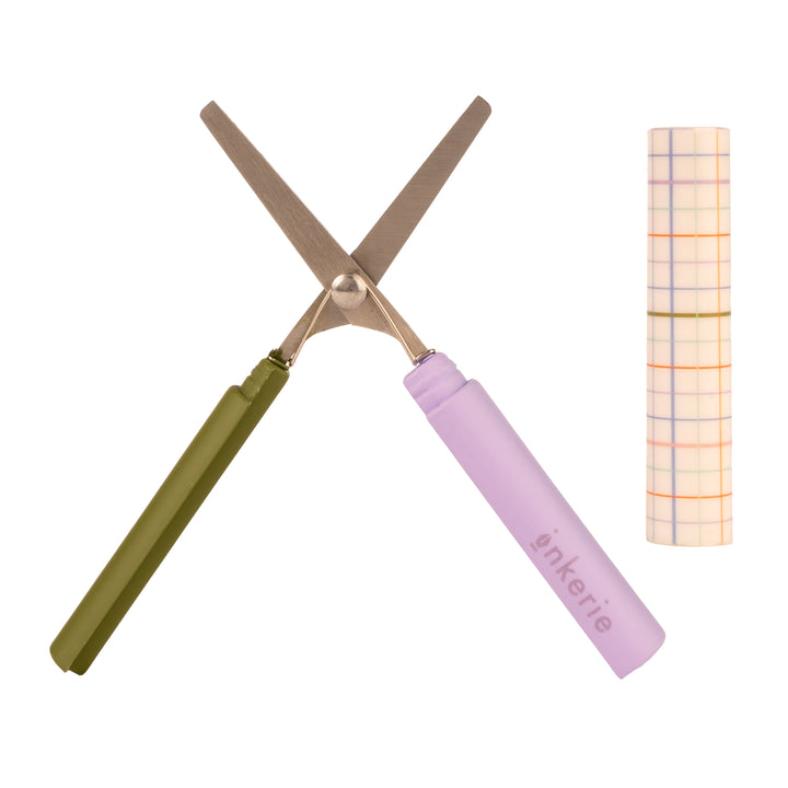 Small scissors with purple and green handles, and gold blades, next to a plaid carrying case.