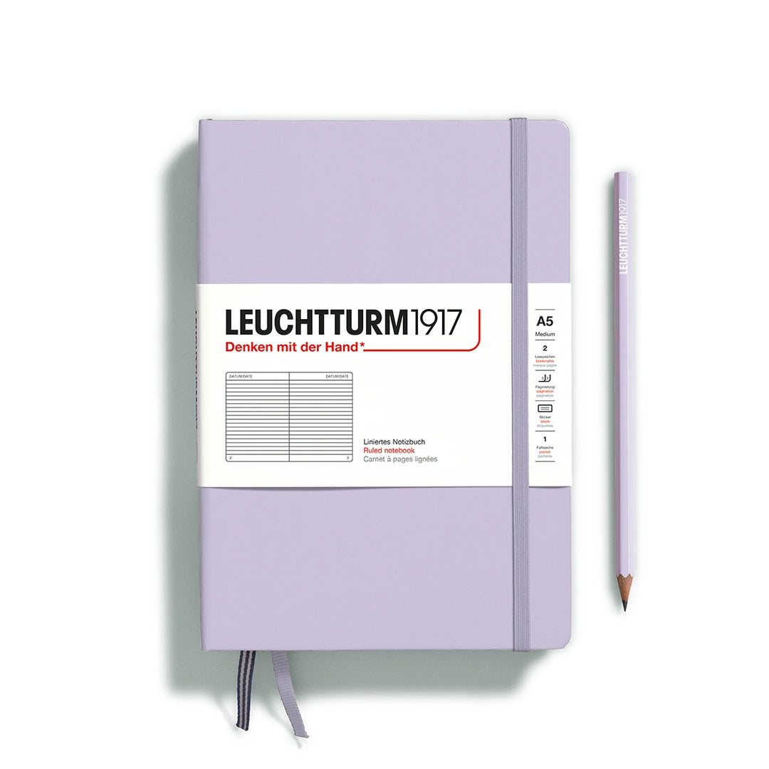 A lilac Leuchtturm1917 A5 ruled page pocket notebook with a white front label and lilac elastic closure,  next to a lilac Leuchtturm1917 pencil.
