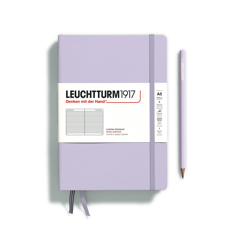 A lilac Leuchtturm1917 A5 ruled page pocket notebook with a white front label and lilac elastic closure,  next to a lilac Leuchtturm1917 pencil.