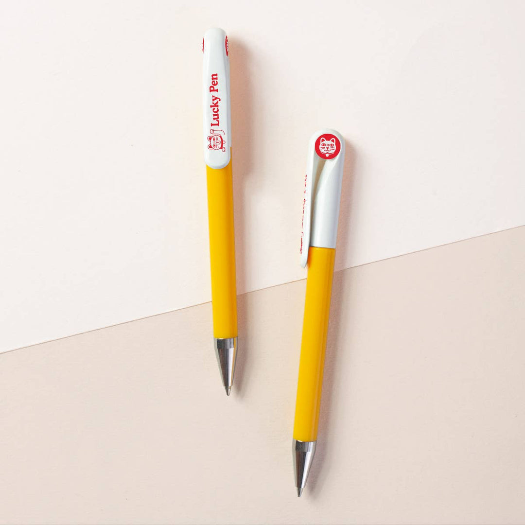 Two sides of a yellow barrel with white top retractable ballpoint pen with silver tips. One side shows the word 'Lucky Pen' with a cat at one end, and the other side has a circular red cap insert with an image of a cat head.