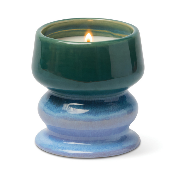 Lit candle in a curvaceous ceramic vessel in colors fading from green to blue 