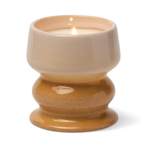 Lit candle in a curvaceous ceramic vessel in colors fading from off white to orange