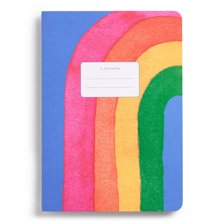 Blue notebook with a rainbow arch, partly off the cover's edge, and a white label in the center.