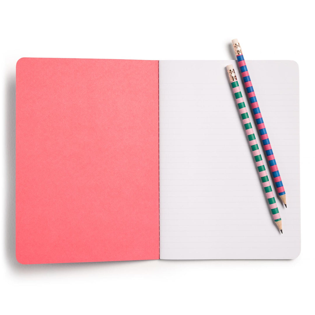 Open notebook with solid orange-pink inside cover and lined white pages. Two pencils lie on top.