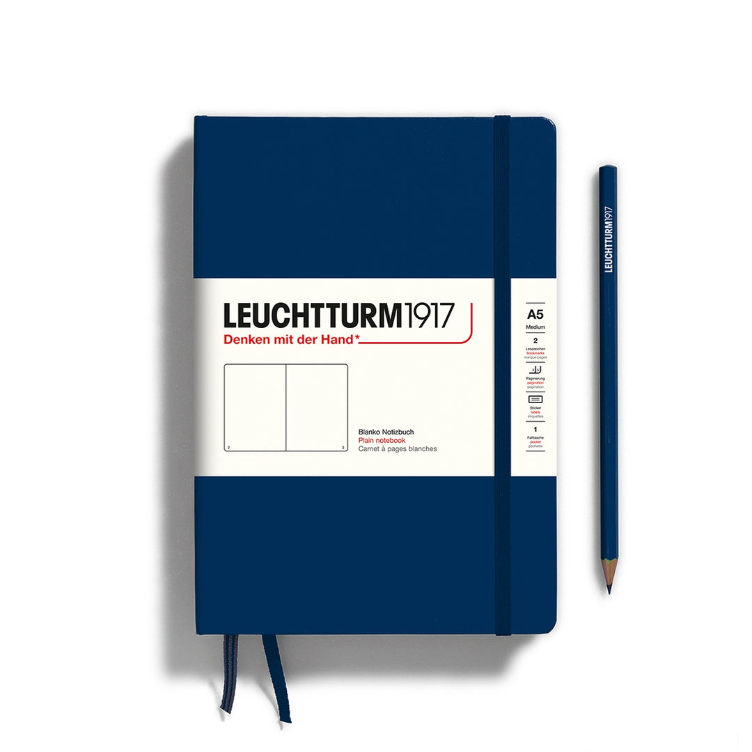 A navy Leuchtturm1917 A5 plain page pocket notebook with a white front label and navy elastic closure,  next to a navy Leuchtturm1917 pencil.