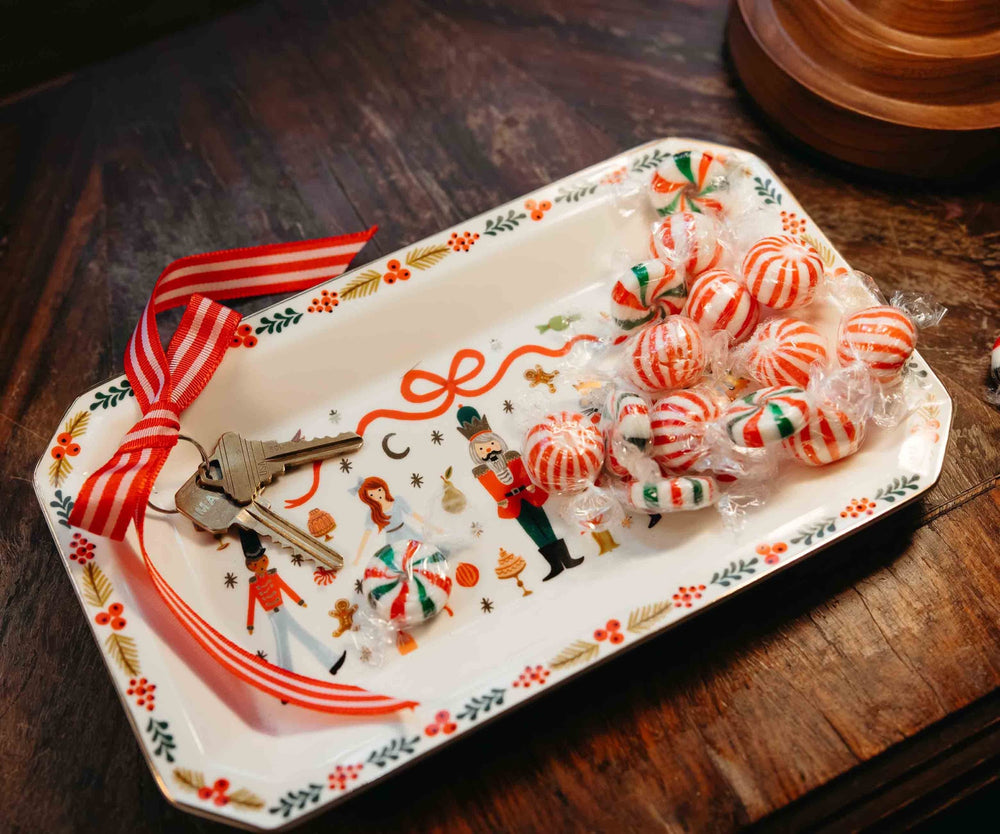Decorative tray with candy, keys, and a ribbon on a wooden table.