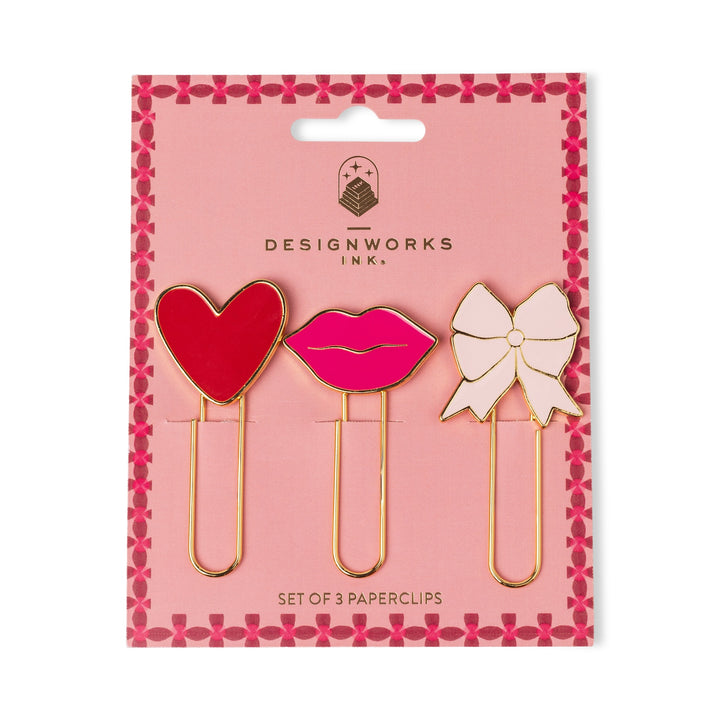 Set of three paperclips shaped like a heart, lips, and a bow on pink cardboard backing.