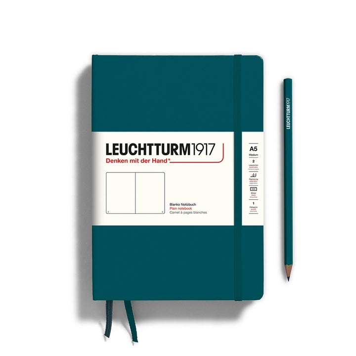 A pacific green Leuchtturm1917 A5 plain page pocket notebook with a white front label and pacific green elastic closure,  next to a pacific green Leuchtturm1917 pencil.
