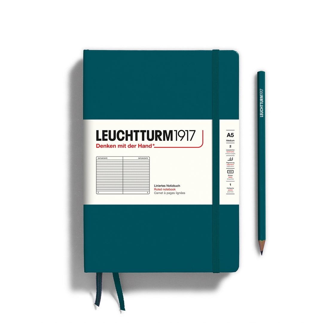 A pacific green Leuchtturm1917 A5 ruled page pocket notebook with a white front label and pacific green elastic closure,  next to a pacific green Leuchtturm1917 pencil.