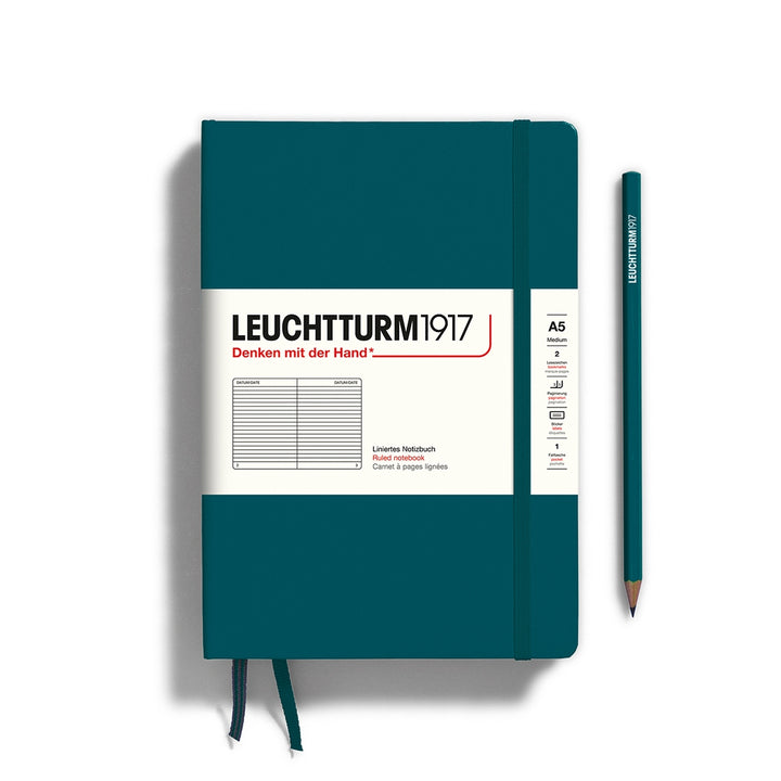 A pacific green Leuchtturm1917 A5 ruled page pocket notebook with a white front label and pacific green elastic closure,  next to a pacific green Leuchtturm1917 pencil.