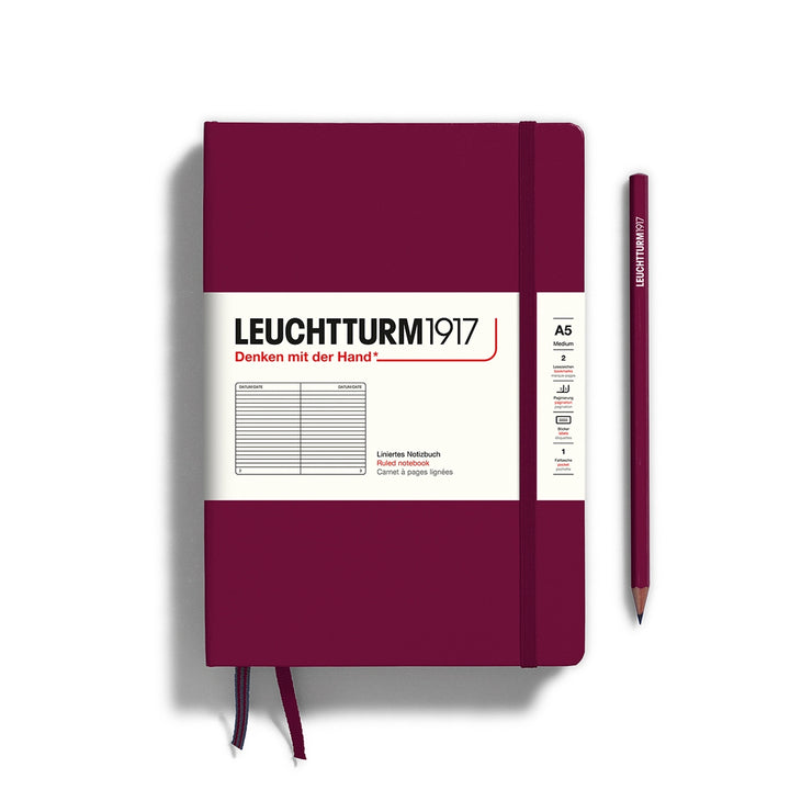 A port red  Leuchtturm1917 A5 ruled page pocket notebook with a white front label and port red elastic closure,  next to a port red Leuchtturm1917 pencil.