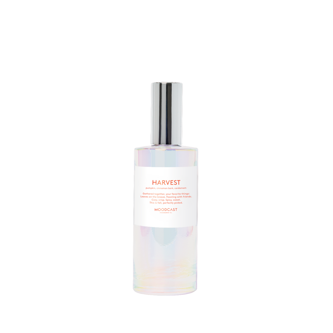 MOODCAST HARVEST Room + Linen spray in a clear bottle with an iridescent finish, a white label with orange text, and a reflective silver cap.