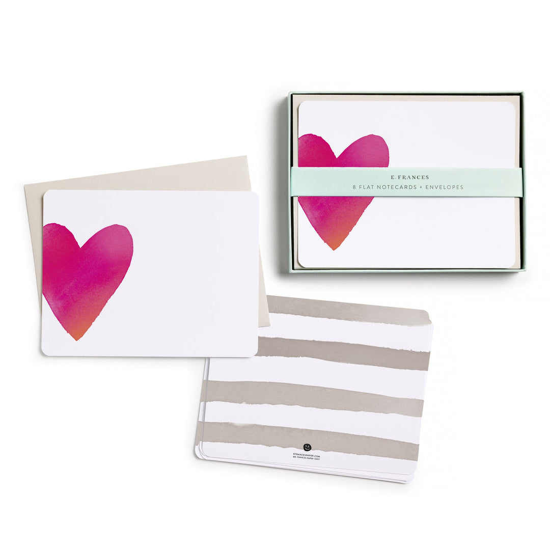 The box of cards, with belly band, next to two stacks of cards, one showing the front, with a large red heart on the left side, and the other the back, with four gray stripes.