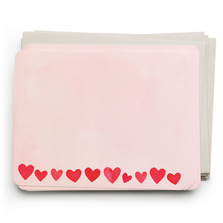 Stack of cards with red hearts across the bottom of a light pink card atop light gray envelopes.