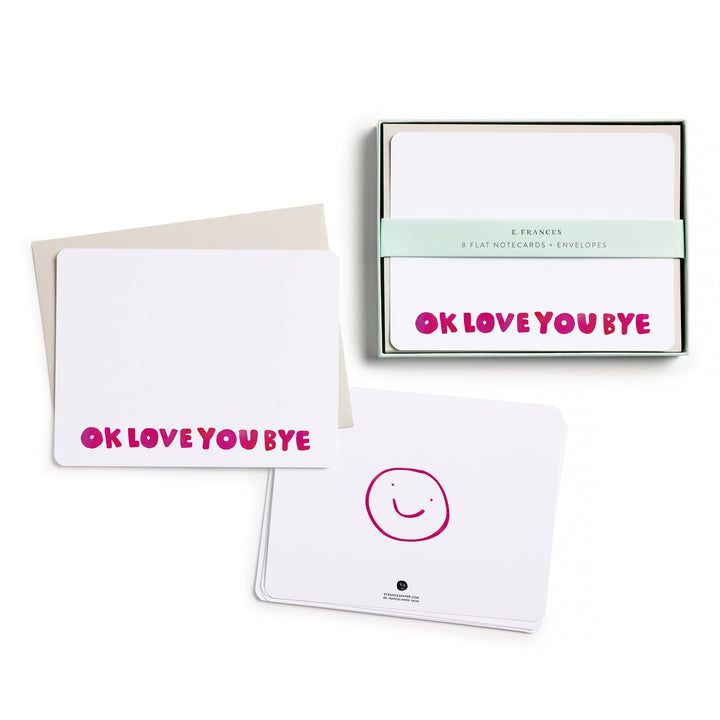 The box of cards, with belly band, next to two stacks of cards, one showing the front, with "OKLOVEYOUBYE" in red across the bottom, and the other the back, with a smiley face drawn in red.
