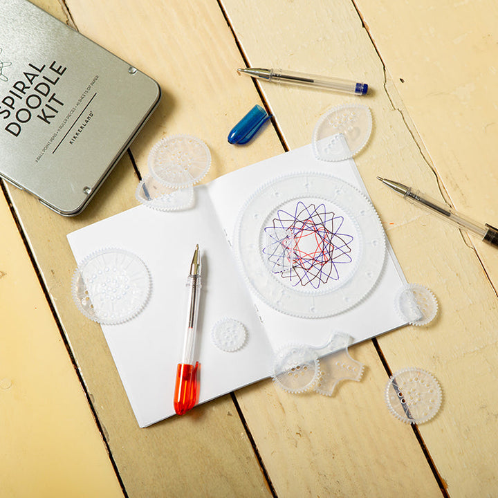 Components of the spiral doodle kit with template wheels of different sizes, pens, and a completed design.