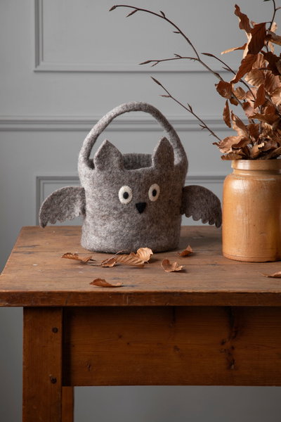 Bat basket on a wooden table next to a vase with fall leaves.