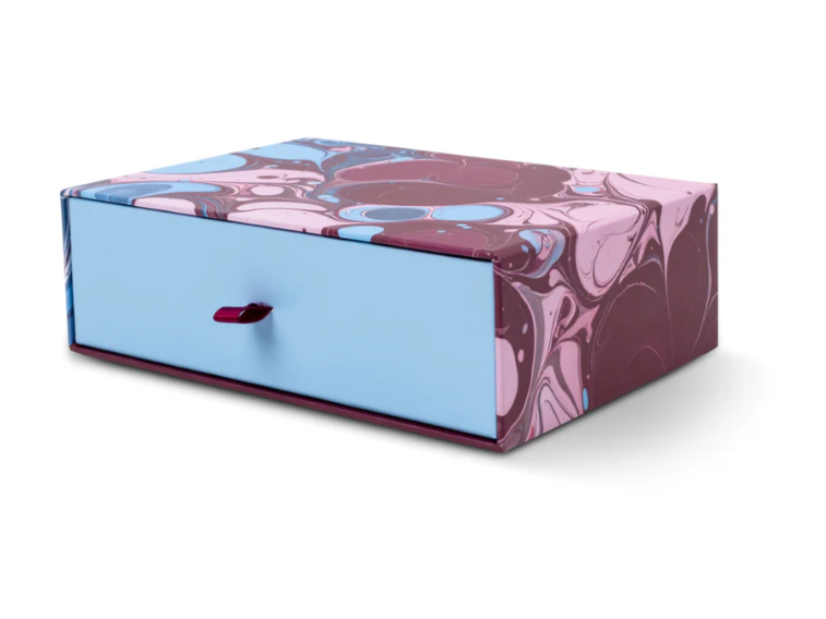 A rectangular storage box with one front drawer, featuring a marbled pattern in pink, purple, and blue on the top and sides, with a solid light blue drawer front and a small dark red pull handle.