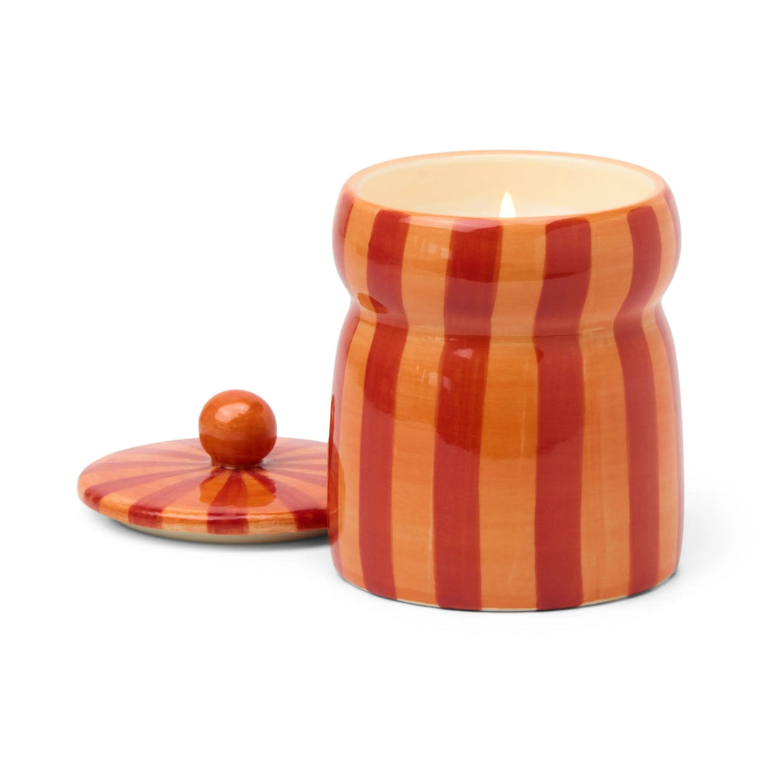 Ceramic candle holder with red and orange vertical stripes next to its lid.
