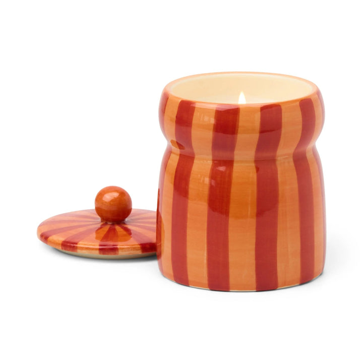 Ceramic candle holder with red and orange vertical stripes next to its lid.
