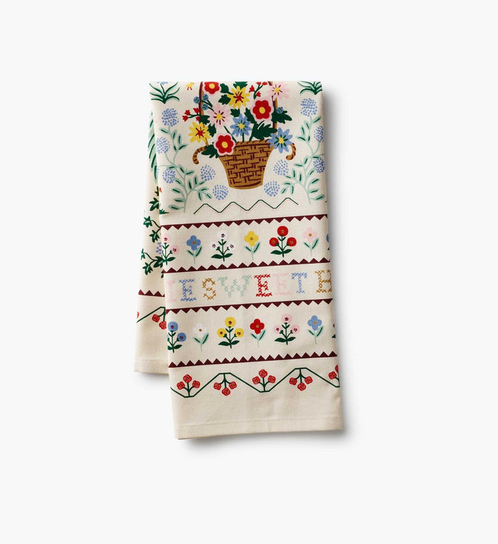 Folded tea towel with floral patterns and text in a cross-stitch pattern.