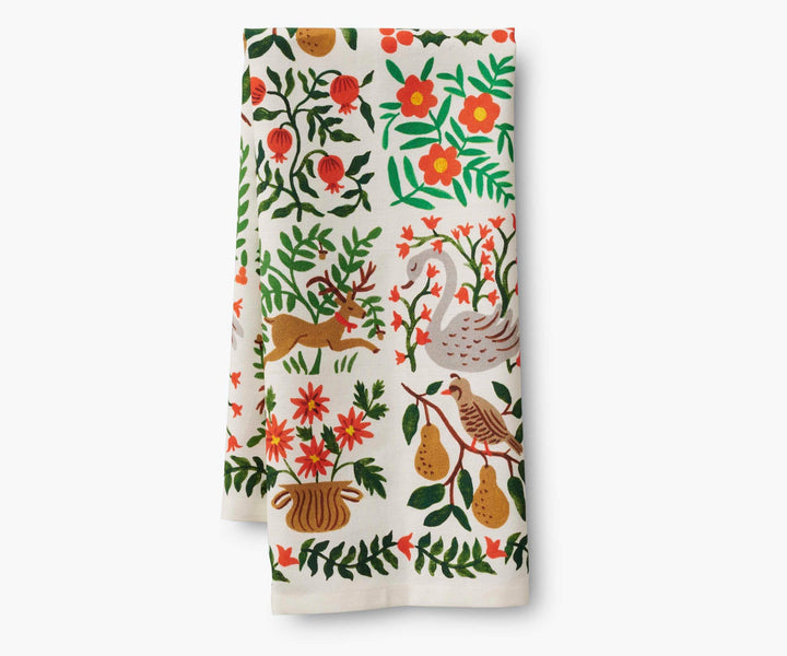Folded tea towel with floral and nature-themed illustrations of  a swan, deer, partridge in a pear tree, persimmons and flowers.