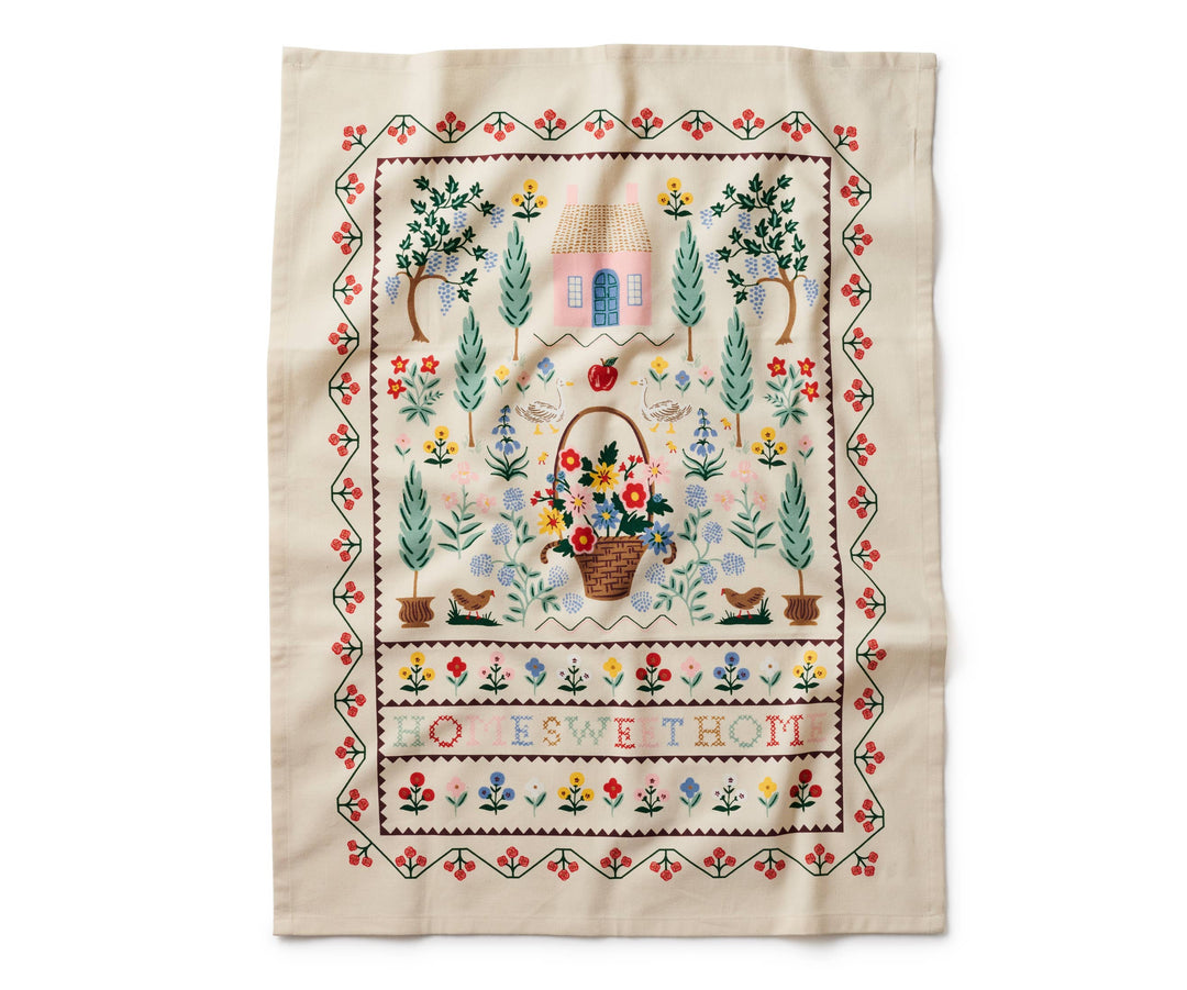 Towel fully open with a red and green border surrounding a garden scene and the text "Home Sweet Home" in cross-stitch pattern.