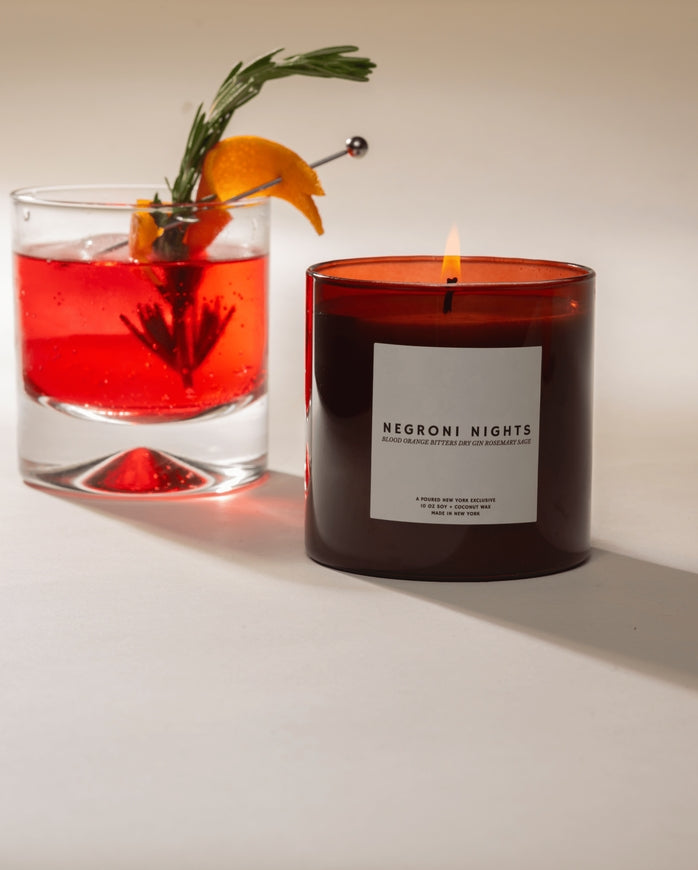 Candle labeled 'Negroni Nights' next to a negroni cocktail with an orange and rosemary garnish.