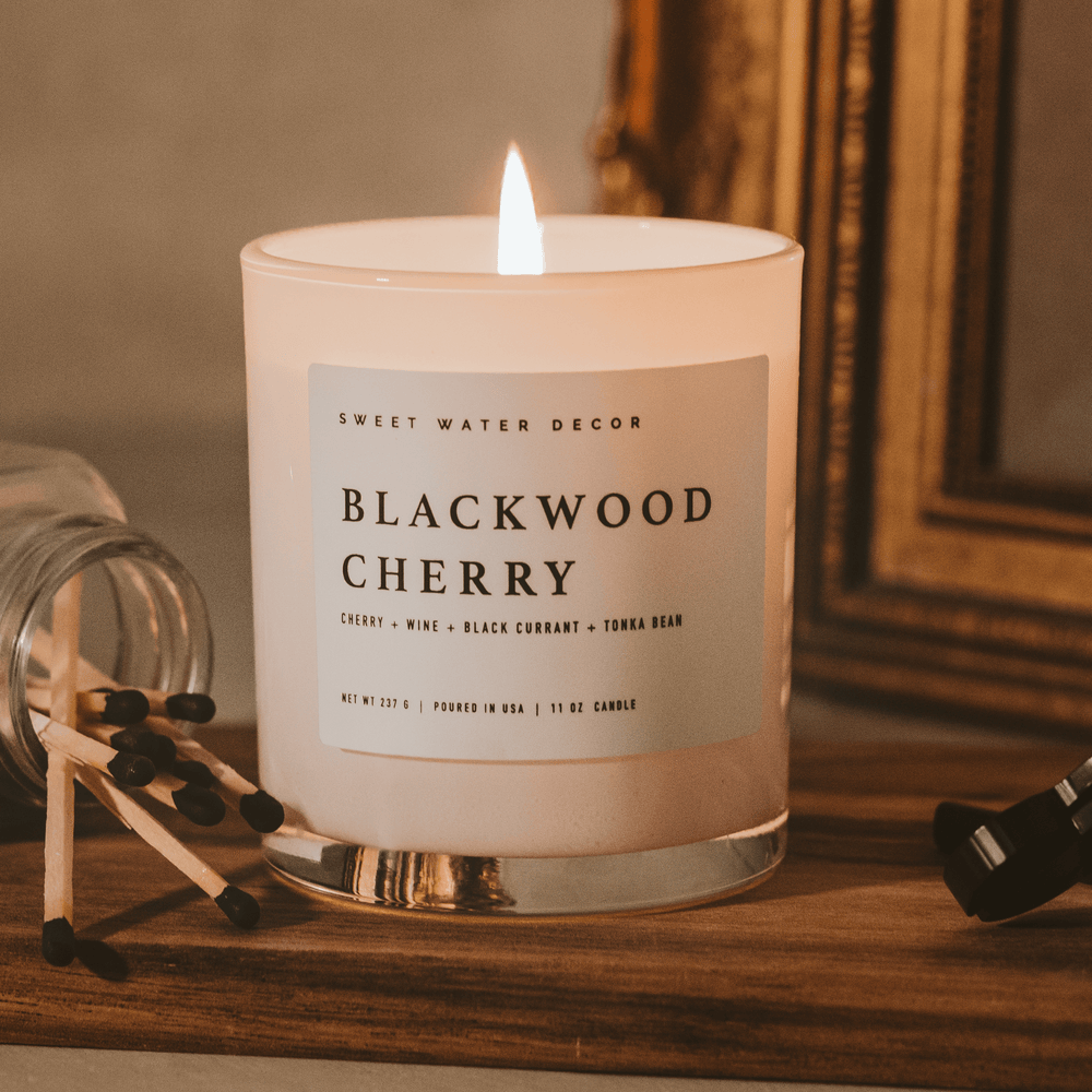 Lit candle on  a desk next to matches and a framed mirror.