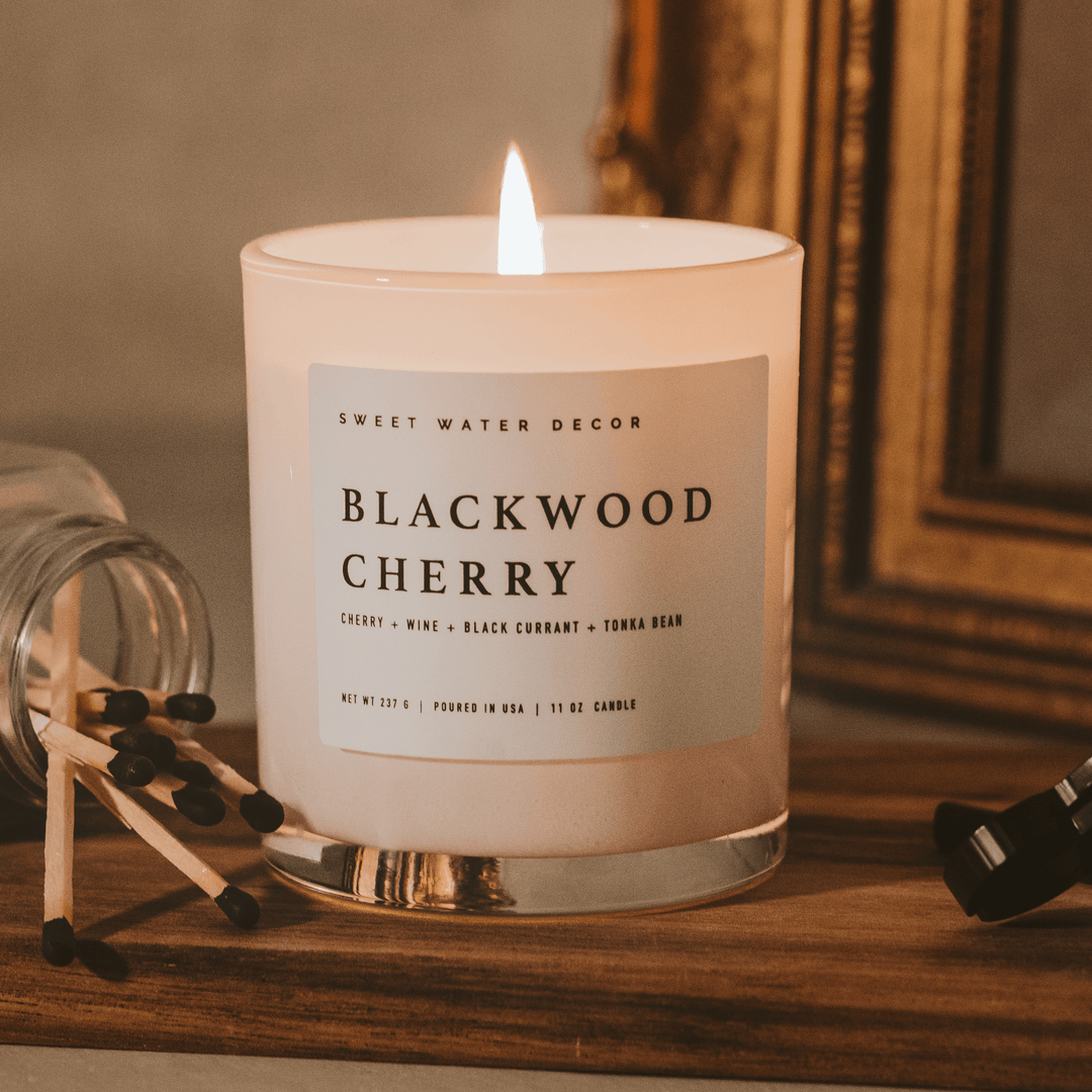 Lit candle on  a desk next to matches and a framed mirror.