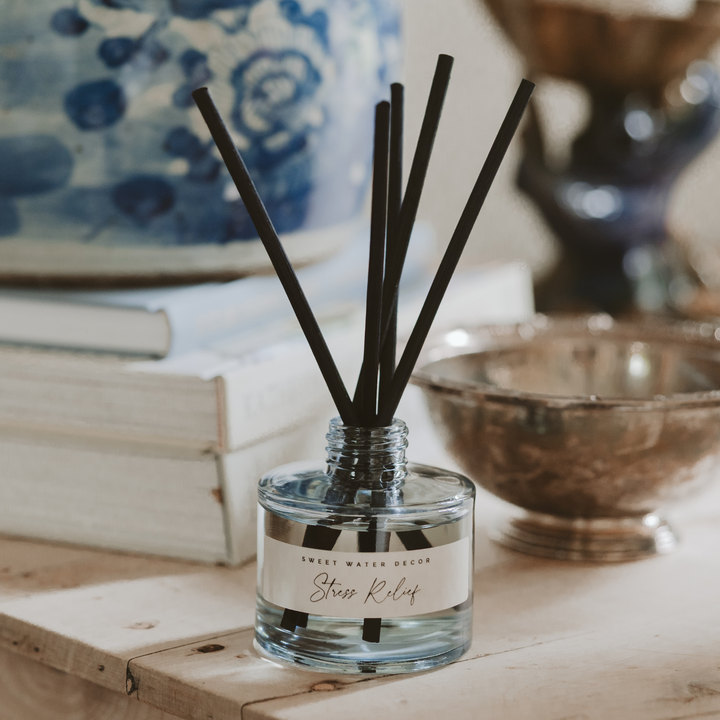 Blue tinted glass jar with five black reeds on a table with books and a bowl.
