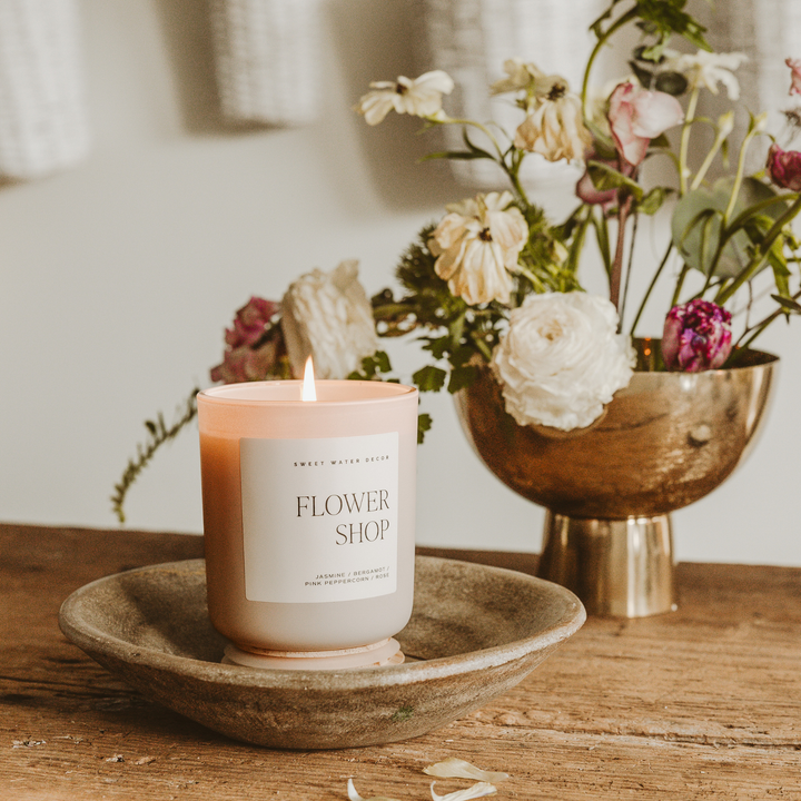 Scented soy candle in a white matte glass container with wooden lid. Label is Flower Shop Jasmine / Pink Peppercorn / Bergamot / Rose