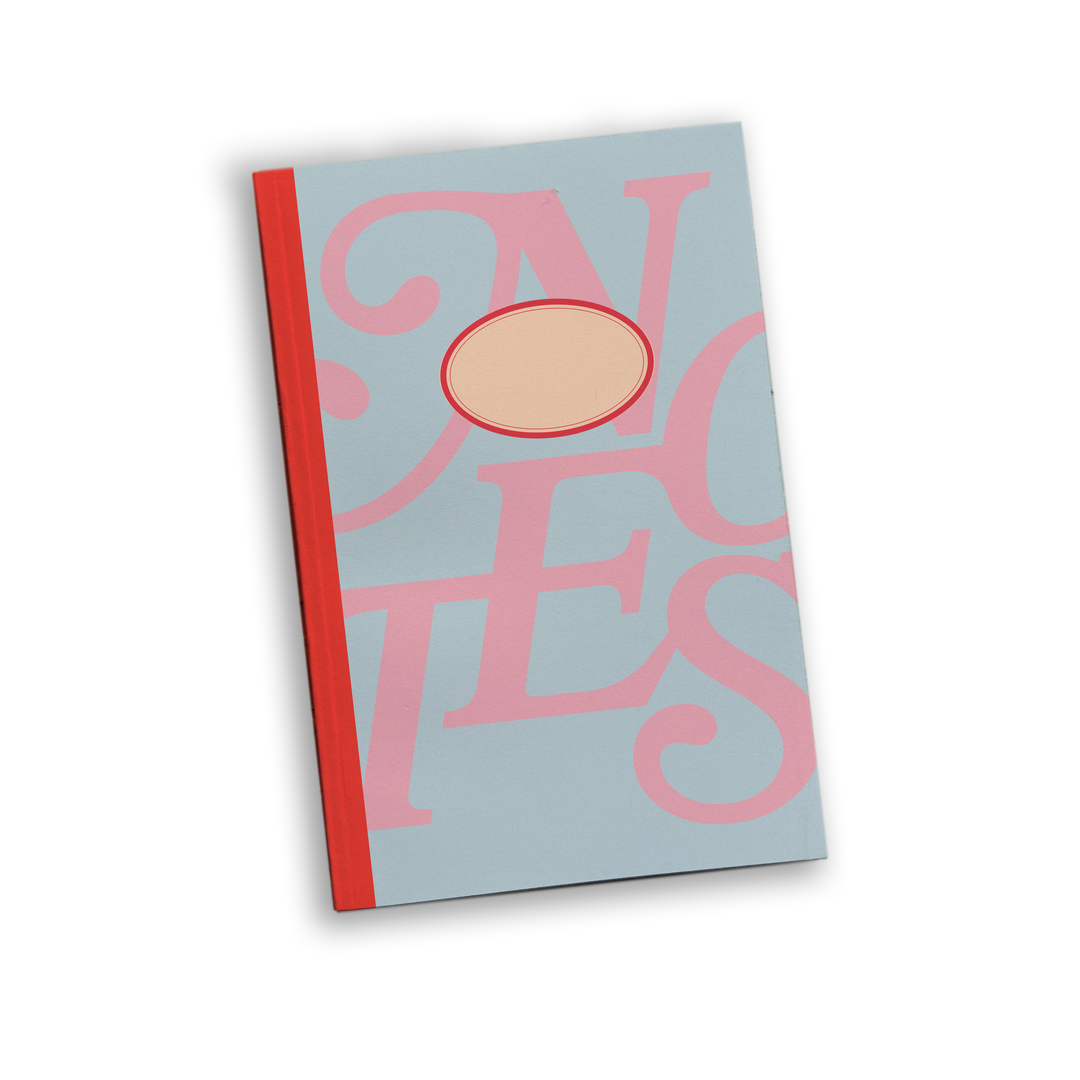A notebook with a light blue cover featuring large pink typography and a central oval cutout, bound with a red spine and red trim.