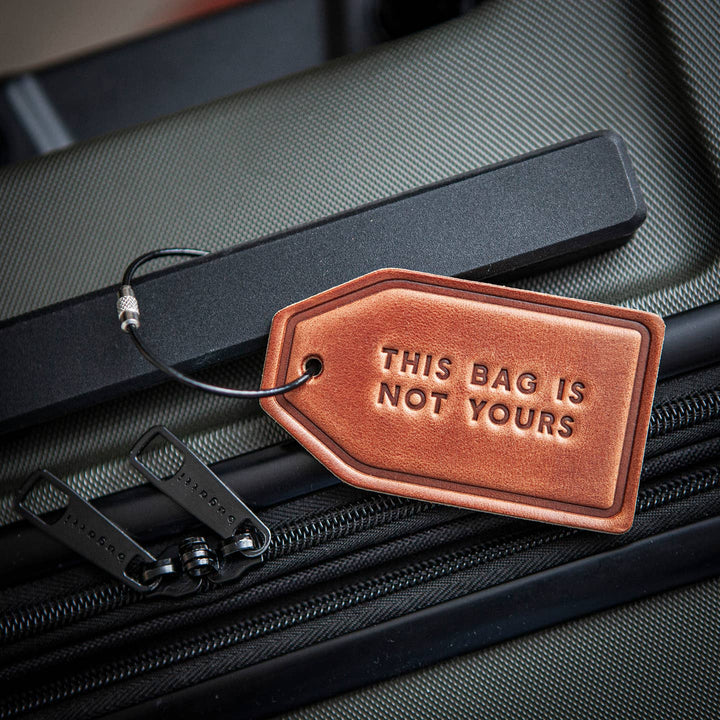 Brown leather luggage tag with 'This Bag is Not Yours' text on a black suitcase.