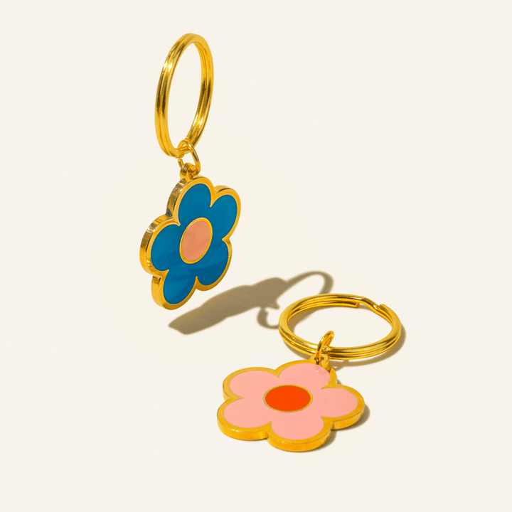 Gold key ring with enamel daisy-shaped fob, one side blue, the other pink, encircled in gold. 