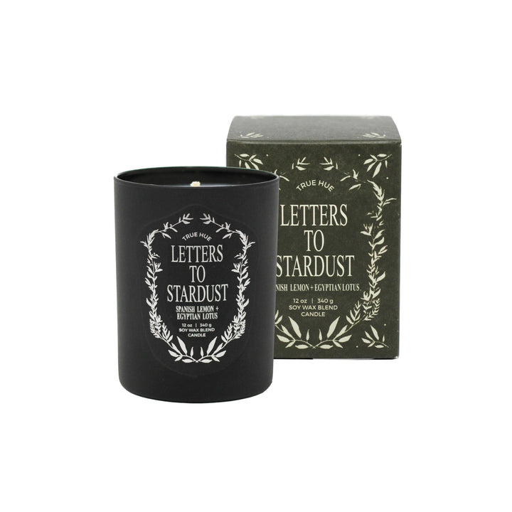 Black candle with 'Letters to Stardust' lettering surrounded by a laurel wreath, next to its box with the same image.