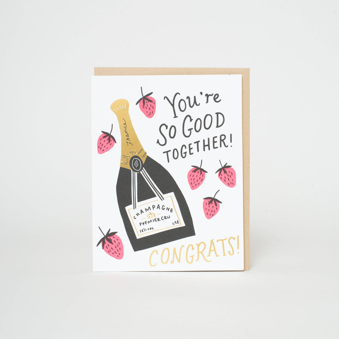 Black and gold champagne bottle with half a dozen strawberries around it. Hand drawn text in black on white cardstpcl/